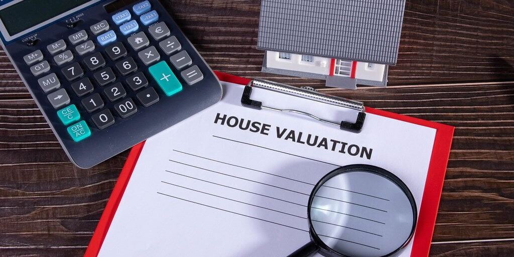 House valuation document with small family house, calculator and magnifying glass on wooden table
