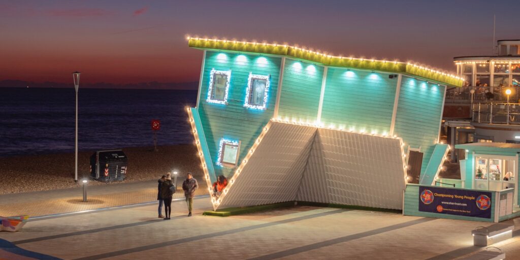 upside down house, a building with lights on it next to the ocean