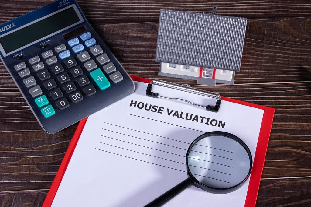 House valuation document with small family house, calculator and magnifying glass on wooden table