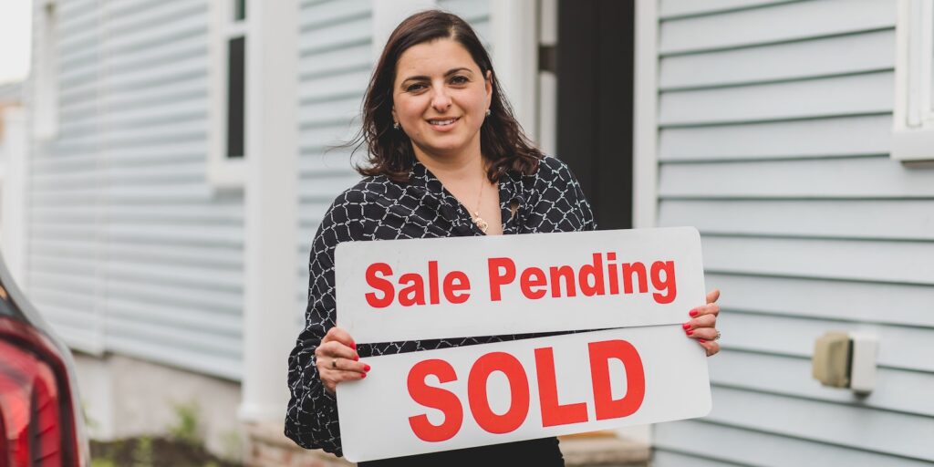 short sale, Real Estate Agent Standing in Black Printed Blouse Holding a Sale Pending Signage